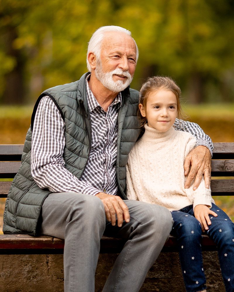 A grandfather and grandaughter sitting on a park bench
